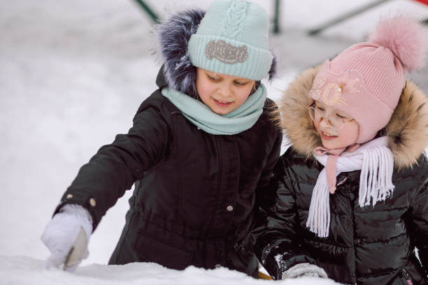 meninas caminha ao ar livre no dia de inverno nevando no parque - playground snow winter little girls - fotografias e filmes do acervo