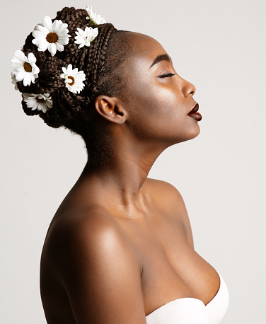 Beauty Profile of African American Woman with White Chamomile Flowers in Black Hair Braids. Fashion Portrait of Dark Skin Model over White Studio Background. Wedding Make up and Bride Cornrows Hairstyle
