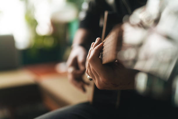 Musician playing his guitar and composing some new music at home. He is sitting on the sofa in the living room.