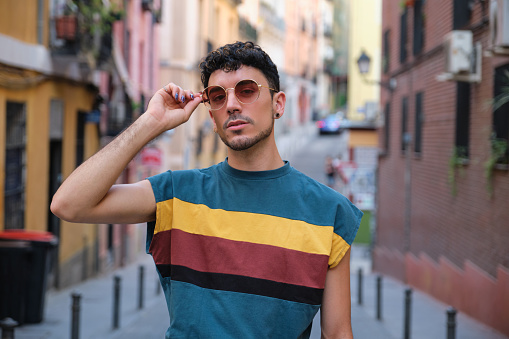 Young caucasian man with long false nails posing with his sunglasses looking at camera at street.