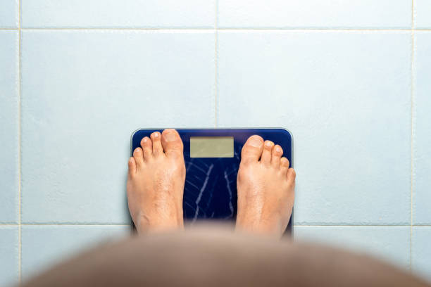 Man looks down at his belly while standing on a weight scale. stock photo