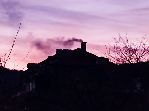 smoke from the chimney on the roof of the house against the sunset purple sky.
