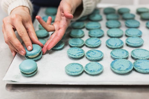 Unrecognizable pastry chef making macarons in pastry shop.