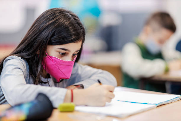istock A schoolgirl writing down answers in notebook in school during covid. 1387244615