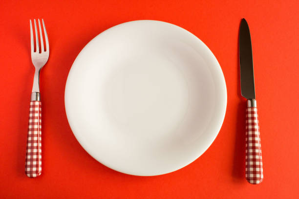istock White plate with  knife and fork on the red  background. Top view. Copy space. 1387246811