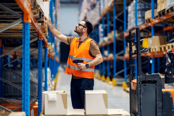 un répartiteur avec un scanner à la main regardant les boîtes sur les étagères de l’entrepôt. - freight transportation warehouse manufacturing shipping photos et images de collection