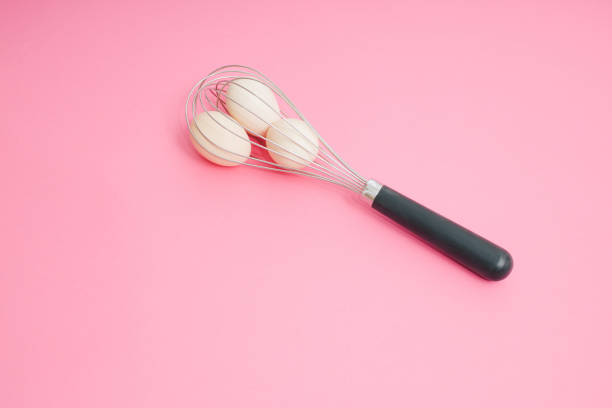 istock Whisk and raw eggs on pastel pink. Light banner background, copy space for text. Culinary mixer, whipping egg white and yolk, preparing and mixing cream. 1387247467