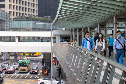 Hong Kong - March 18, 2022 : Pedestrians wearing face masks walk on a footbridge in Central, Hong Kong. Hong Kong's compulsory mask-wearing rules cover all public areas.