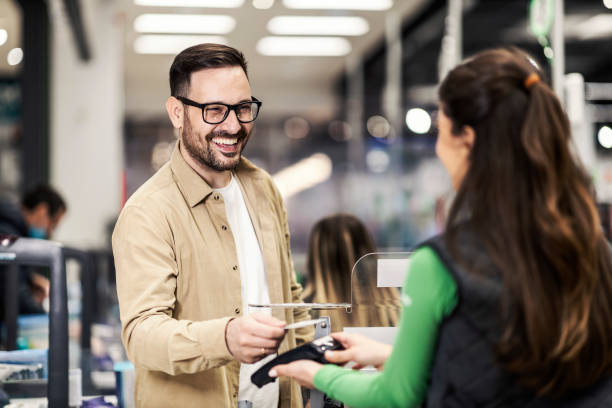 a happy customer paying at checkout with credit card in supermarket. - detailhandel beroep fotos stockfoto's en -beelden