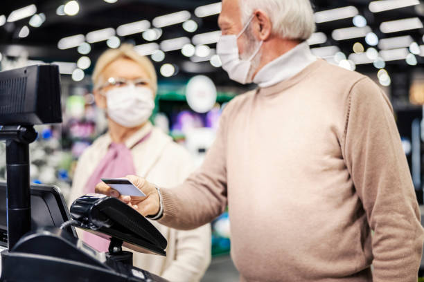 A senior couple at self-service cash register paying with credit card during corona virus. Grandparents at self-service cash register paying with credit card at supermarket during covid 19. consumer confidence photos stock pictures, royalty-free photos & images