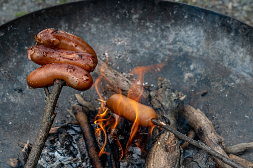 Barbecue on fire. Sausage heating above the campfire in Switzerland.