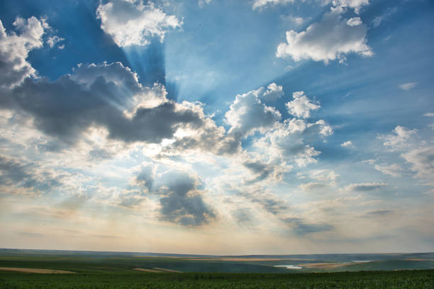 Golden rays of sunshine breaking trough the white clouds and gently touching the green meadow.