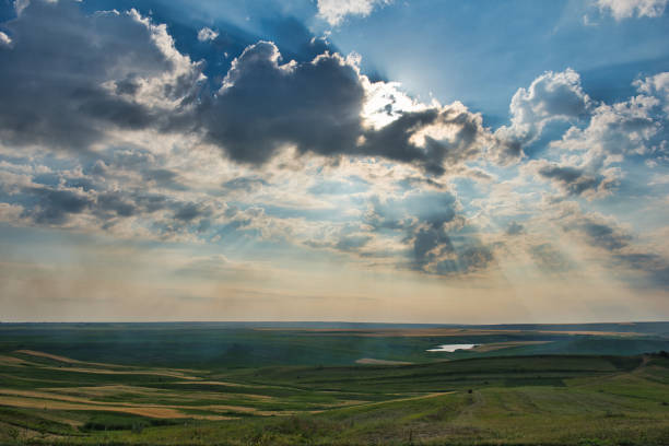 Breathtaking view of rays of sun breaking trough the fluffy white clouds and gently touching the meadow