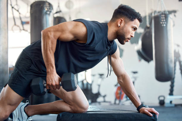 foto de un joven deportista haciendo ejercicio con una mancuerna en un gimnasio - culturismo fotografías e imágenes de stock