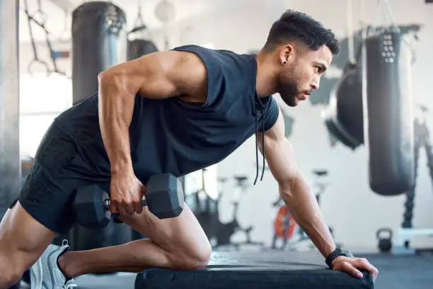 Photo of Shot of a sporty young man exercising with a dumbbell in a gym