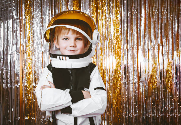 Child in fancy dress of astronaut pilot costume having fun at masquerade party in festive background with foil curtain decorations. Kids birthday party, Halloween, New Year, Celebration, Holiday. Child in fancy dress of astronaut pilot costume having fun at masquerade party in festive background with foil curtain decorations. Kids birthday party, Halloween, New Year, Celebration any Holiday. cosmonaut photos stock pictures, royalty-free photos & images