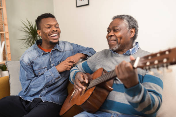 Senior African American playing a guitar and enjoying with his son Portrait of a senior African American man playing a guitar for his son in a visit father and son guitar stock pictures, royalty-free photos & images