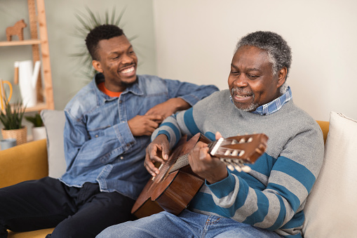 Portrait of a senior African American man playing a guitar for his son in a visit