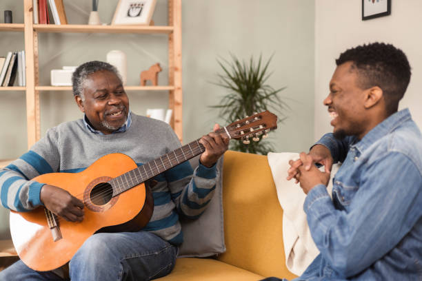 Senior man playing a guitar and amusing his son Portrait of a senior African American man playing a guitar for his son in a visit father and son guitar stock pictures, royalty-free photos & images