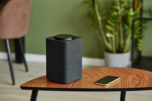 Minimal background image of smart speaker with home AI system on wooden table against green wall, copy space
