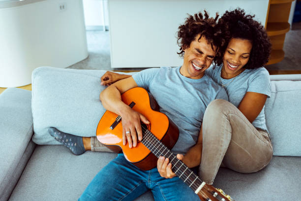 istock Young man plays guitar for young woman on sofa 1387263626