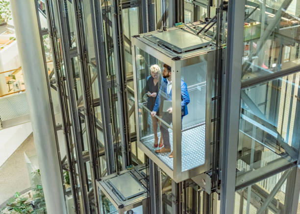 istock Young businesspeople in elevator holding mobile phone and laptop 1387268073