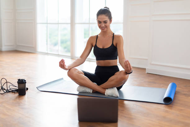 istock Young woman meditating in lotus position on mat with pc 1387268344