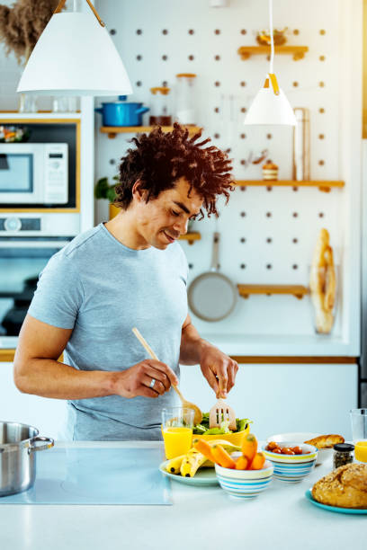 istock Young man standing in kitchen cooking salad for lunch 1387269062
