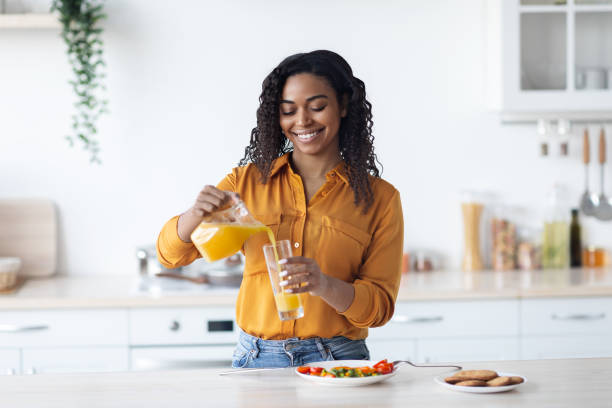 istock Smiling black woman pouring fresh orange juice, kitchen interior 1387269685