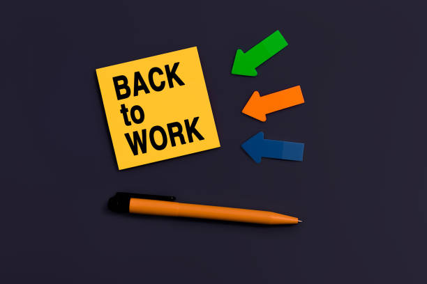 istock Back to work - concept of text on sticky note. Orange square sticky note, pen and colorful arrows on dark blue background, top view 1387271545