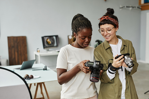 Waist up portrait of two female photographers holding cameras while working in photo studio, copy space