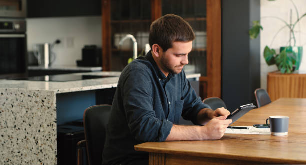 istock Shot of a young man using a digital tablet and going through paperwork at home 1387278541