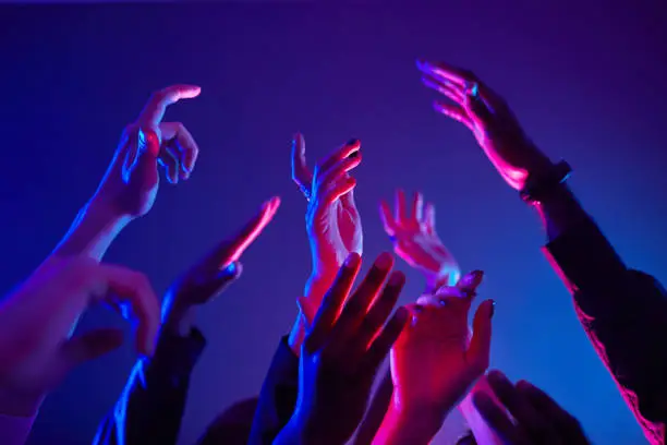 Close up of crowd dancing in club with hands up lit by neon lights, copy space