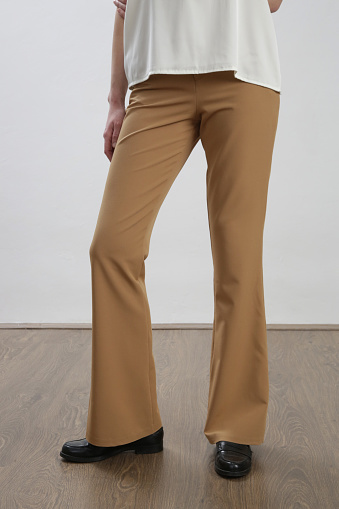 Female model wearing beige tailored trousers. Studio shot.