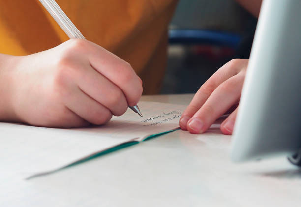 istock A child's hands writing with a pen in a notebook. Online learning, education at home. 1387280460