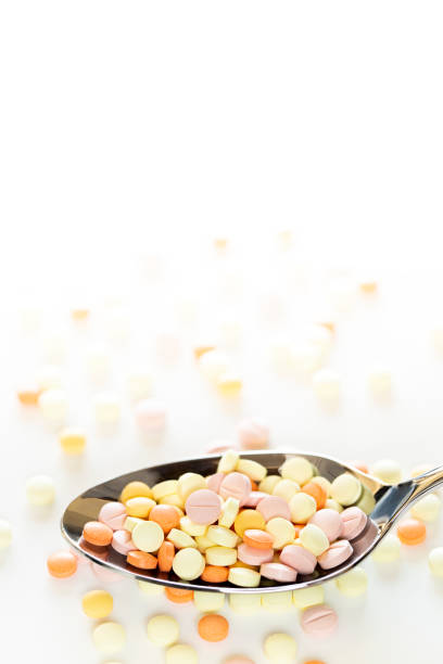 pillules colorées sur la cuillère. - vitamin pill vertical high key photographic effects photos et images de collection
