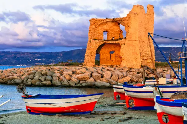 Photo of Picturesque beach scenery with tradtional fishing boats and saracen tower over sunset in Calabria. Landmarks of south Italy