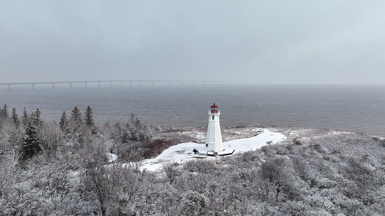 Aerial drone photograph of Cape Jourimain Lighthouse and Confederation Bridge in the background in winter with snow