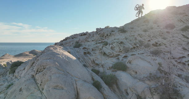 Aerial view of mountain biker on sunny coastal cliffs He carries the bike up the cliff, over the Pacific Ocean top view on people walking and cyclists riding stock pictures, royalty-free photos & images