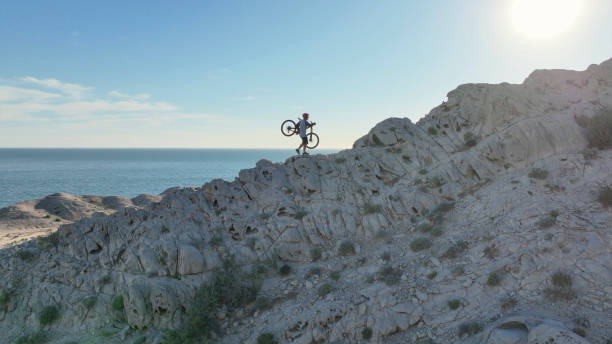 Aerial view of mountain biker on sunny coastal cliffs He carries the bike up the cliff, over the Pacific Ocean top view on people walking and cyclists riding stock pictures, royalty-free photos & images