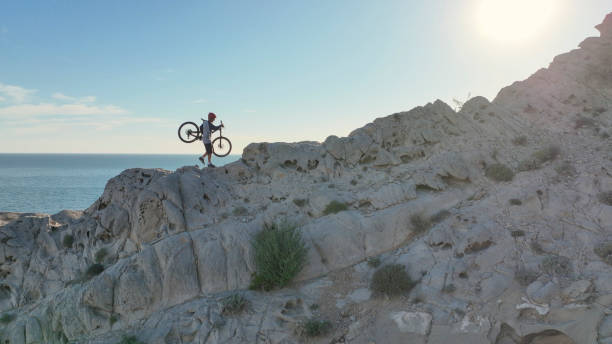 Aerial view of mountain biker on sunny coastal cliffs He carries the bike up the cliff, over the Pacific Ocean top view on people walking and cyclists riding stock pictures, royalty-free photos & images