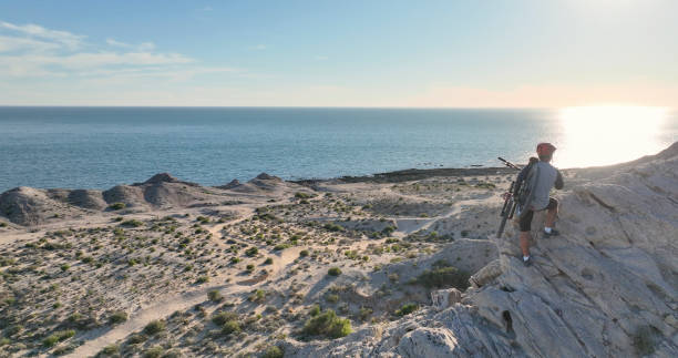 Aerial view of mountain biker on sunny coastal cliffs He carries the bike up the cliff, over the Pacific Ocean top view on people walking and cyclists riding stock pictures, royalty-free photos & images
