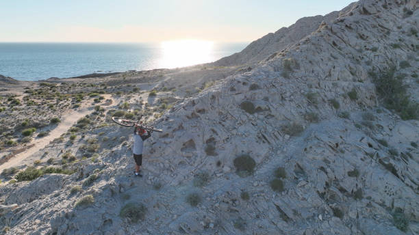 Aerial view of mountain biker on sunny coastal cliffs He carries the bike up the cliff, over the Pacific Ocean top view on people walking and cyclists riding stock pictures, royalty-free photos & images