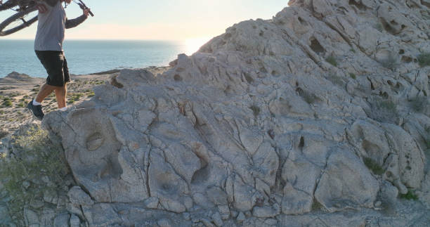 Man carries mountain bike along sunny coastal cliffs He carries the bike on his back, over the Pacific Ocean top view on people walking and cyclists riding stock pictures, royalty-free photos & images