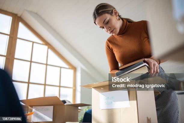 Caring Caucasian Young Woman Packing Toys And Books For Donation Into Cardboard Box Stock Photo - Download Image Now