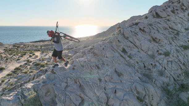 Man carries mountain bike along sunny coastal cliffs He carries the bike on his back, over the Pacific Ocean top view on people walking and cyclists riding stock pictures, royalty-free photos & images