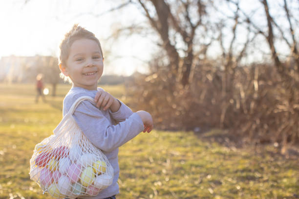 Cute toddler boy, gathering Easter colorful eggs in a basket in the park, springtime
