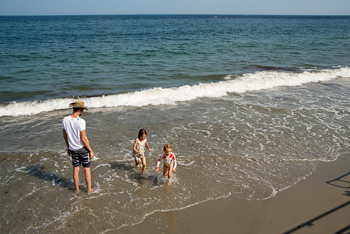 Father and little daughters playing in ocean waves. Dad is in his forties, daughters are 6 and 4 year’s old. Horizontal full length outdoors shot with copy space.