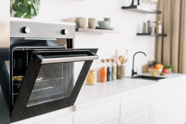 Stylish black oven with open door in kitchen Side view of black oven with open door in modern Scandinavian studio style. Contemporary white wood furniture and kitchenware. Cozy place for cooking oven door stock pictures, royalty-free photos & images