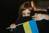 Little girl holding Ukrainian flag hugging her dad